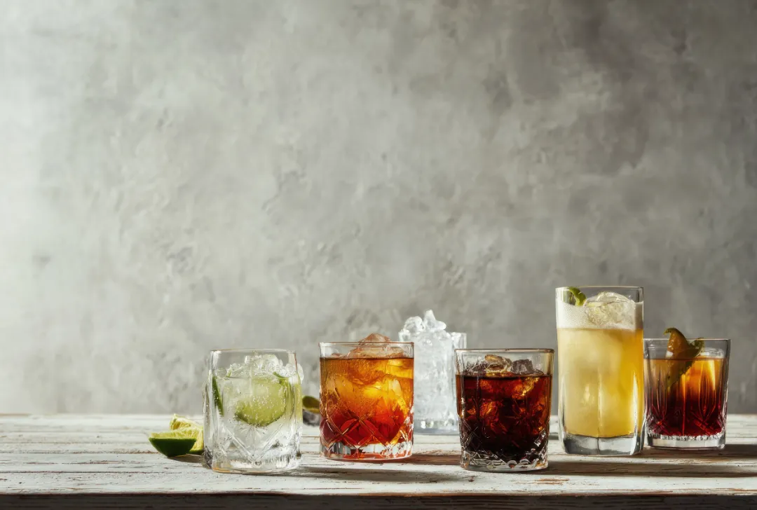 An assortment of colorful cocktails are arranged on a wooden surface in this image.